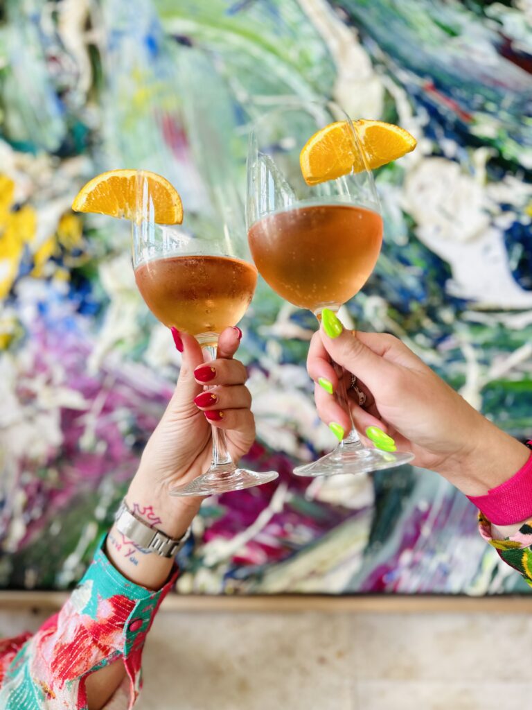 Two hands holding a spritz making a cheers. One of the best Palm Beach Restaurants